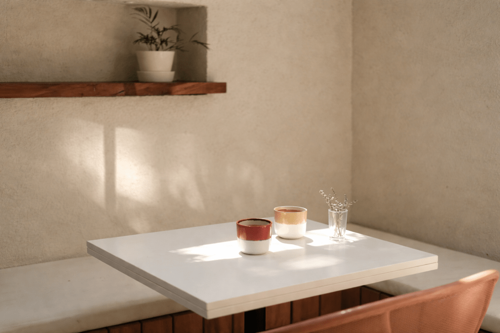 Sunlit café table with two ceramic cups and a small glass vase, lit by soft natural light.